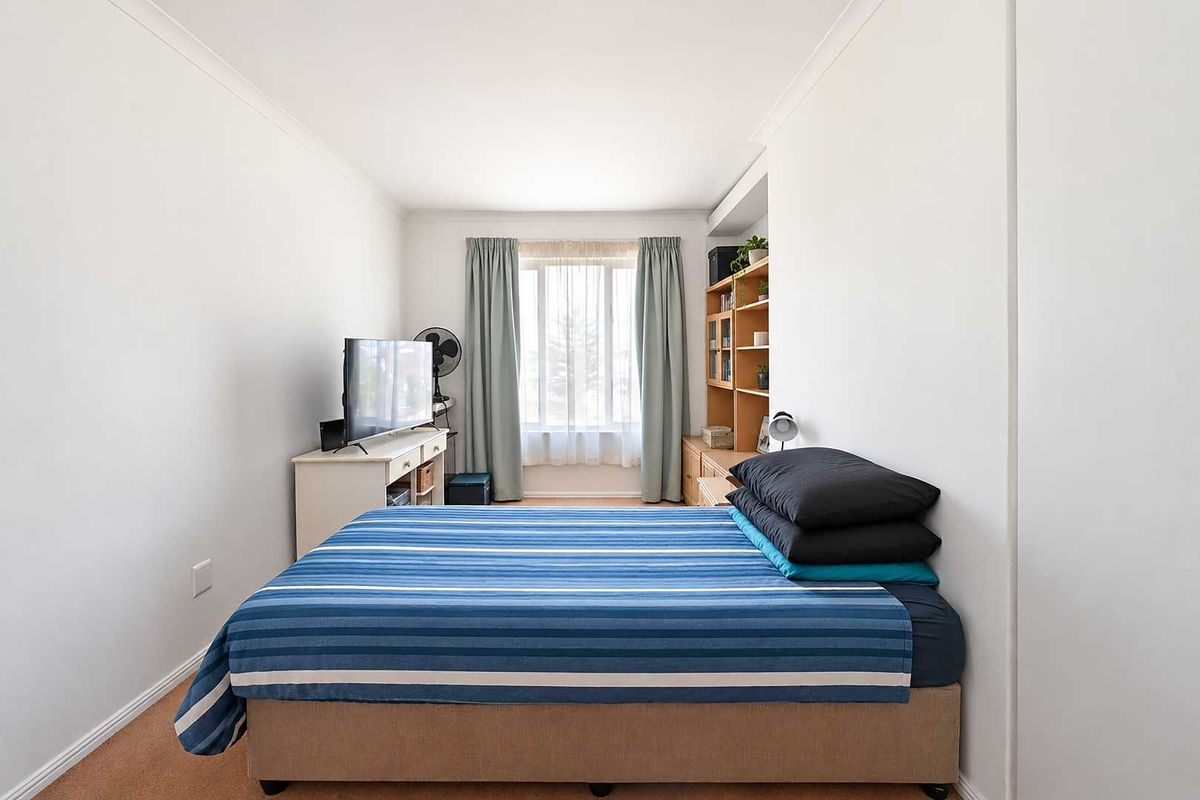 A functional bedroom featuring neutral walls, carpeted flooring, and built-in shelving, providing a comfortable and practical living space.