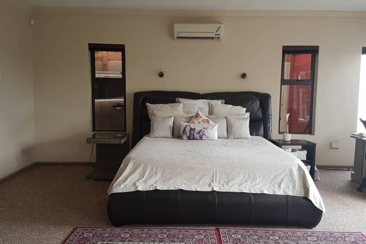 Spacious bedroom featuring neutral carpeting, wall-mounted air conditioning unit, and dual vertical windows providing natural light.