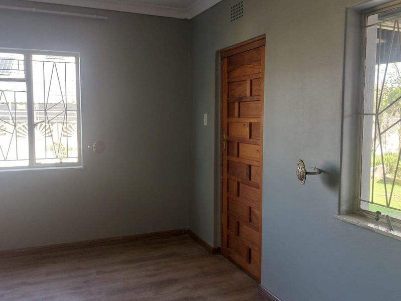 A vacant bedroom featuring laminate flooring, a solid timber door, and windows fitted with security bars.