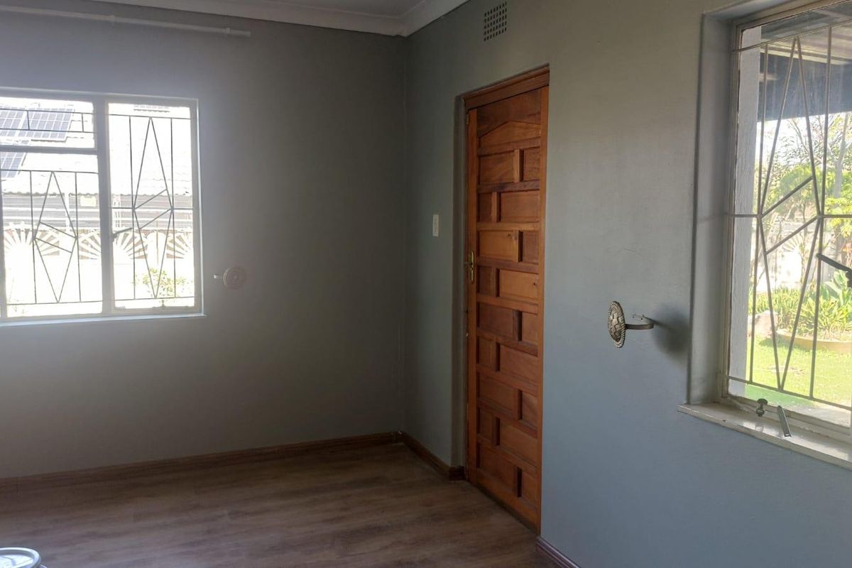 A vacant bedroom featuring laminate flooring, a solid timber door, and windows fitted with security bars.