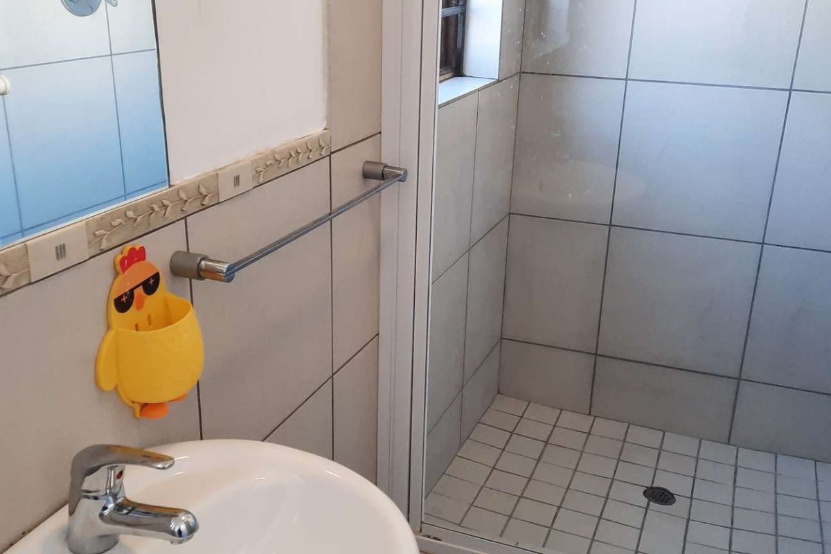 A functional bathroom featuring a shower enclosure, pedestal basin with mixer tap, and tiled finishes throughout.