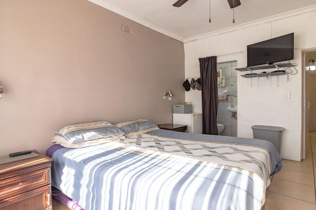 A bedroom featuring tiled flooring, a ceiling fan, and direct access to an en-suite bathroom, showing signs of wear on the walls.