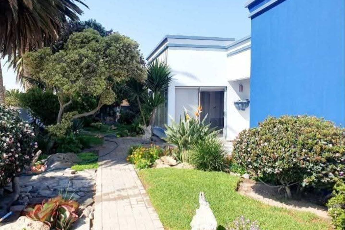 A well-maintained rear garden featuring a paved walkway leading to a sliding glass door entrance, surrounded by established landscaping and shrubs.