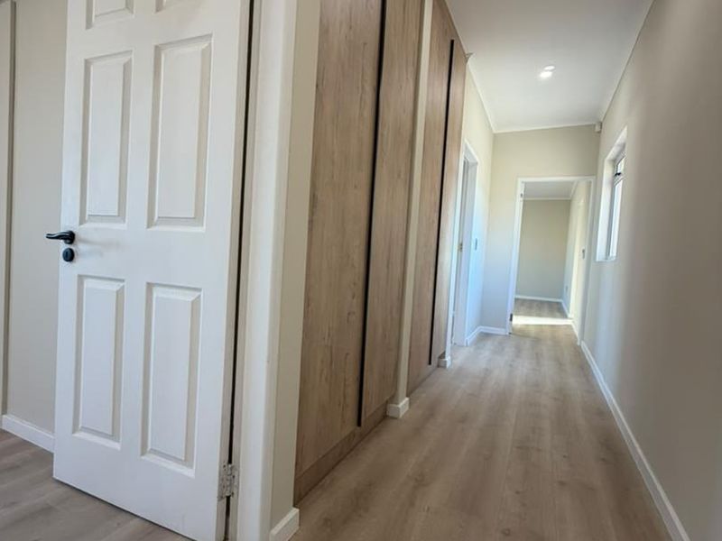 A bright, modern hallway featuring light wood-look laminate flooring, recessed downlights, and floor-to-ceiling built-in cabinetry with a clean, neutral aesthetic.