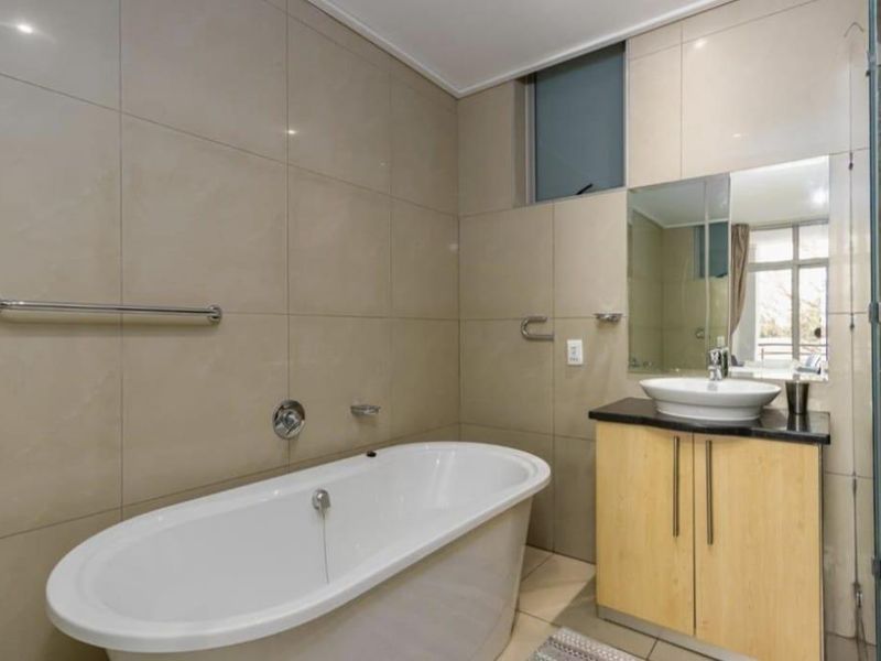 Modern bathroom featuring a freestanding bathtub, vessel sink with vanity cabinet, glass-enclosed shower, and neutral floor-to-ceiling wall tiles.
