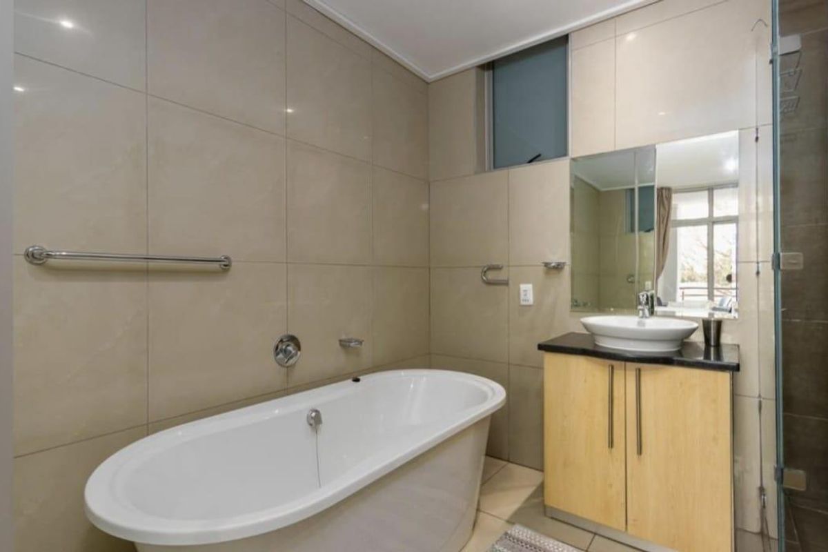 Modern bathroom featuring a freestanding bathtub, vessel sink with vanity cabinet, glass-enclosed shower, and neutral floor-to-ceiling wall tiles.