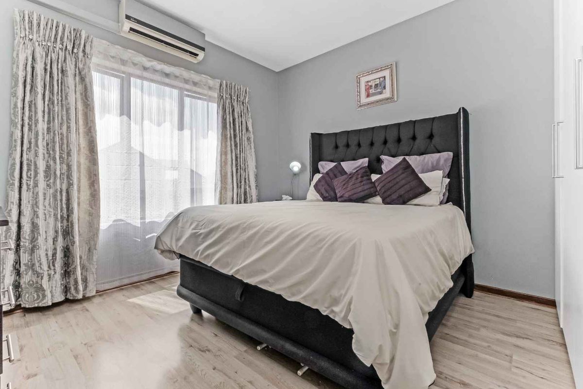 A well-maintained bedroom featuring light wood-look flooring, neutral wall tones, and a wall-mounted air conditioning unit.