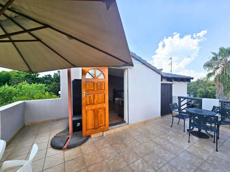 A spacious outdoor balcony featuring tiled flooring, a wooden entrance door, and protective railings, offering a functional space for outdoor relaxation.