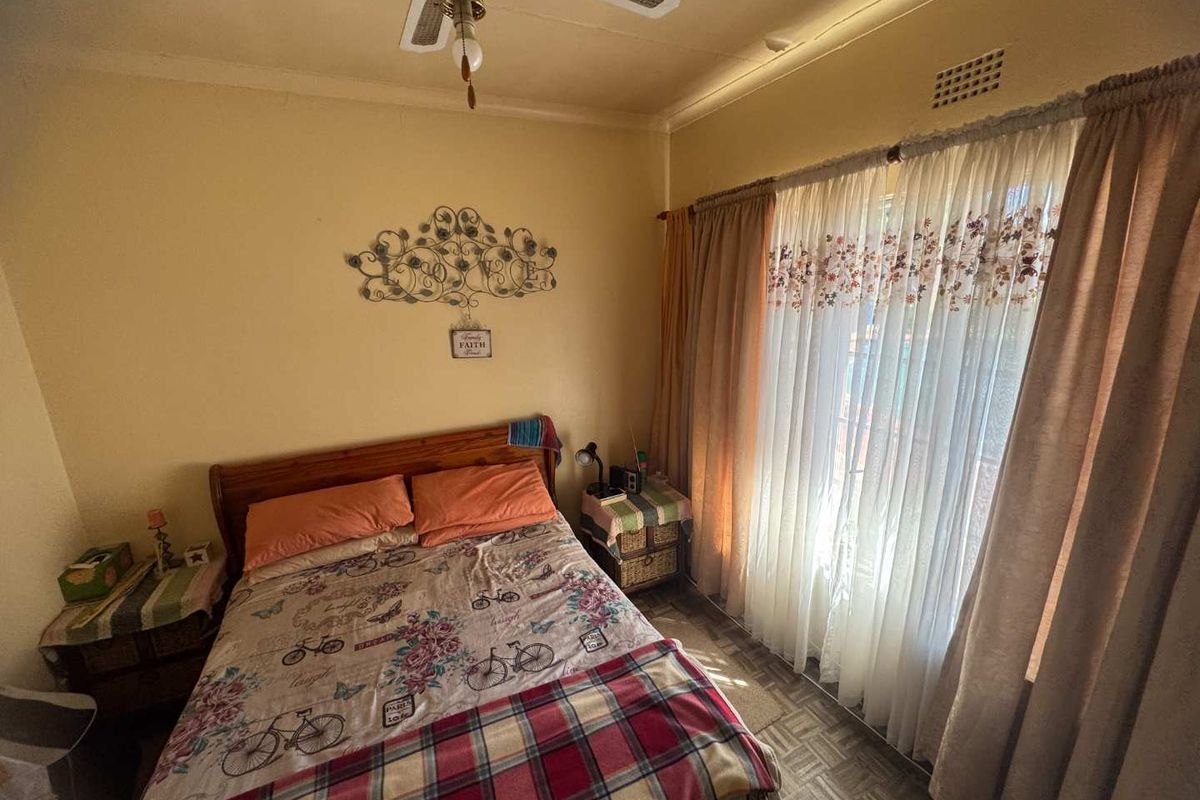 A bedroom featuring a ceiling fan, large window with curtains, and parquet flooring, offering a comfortable and functional living space.