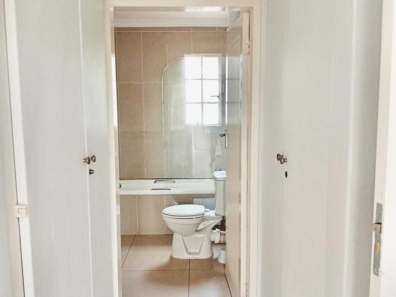 A view through a hallway into a functional bathroom featuring a bathtub, toilet, and neutral wall and floor tiling.