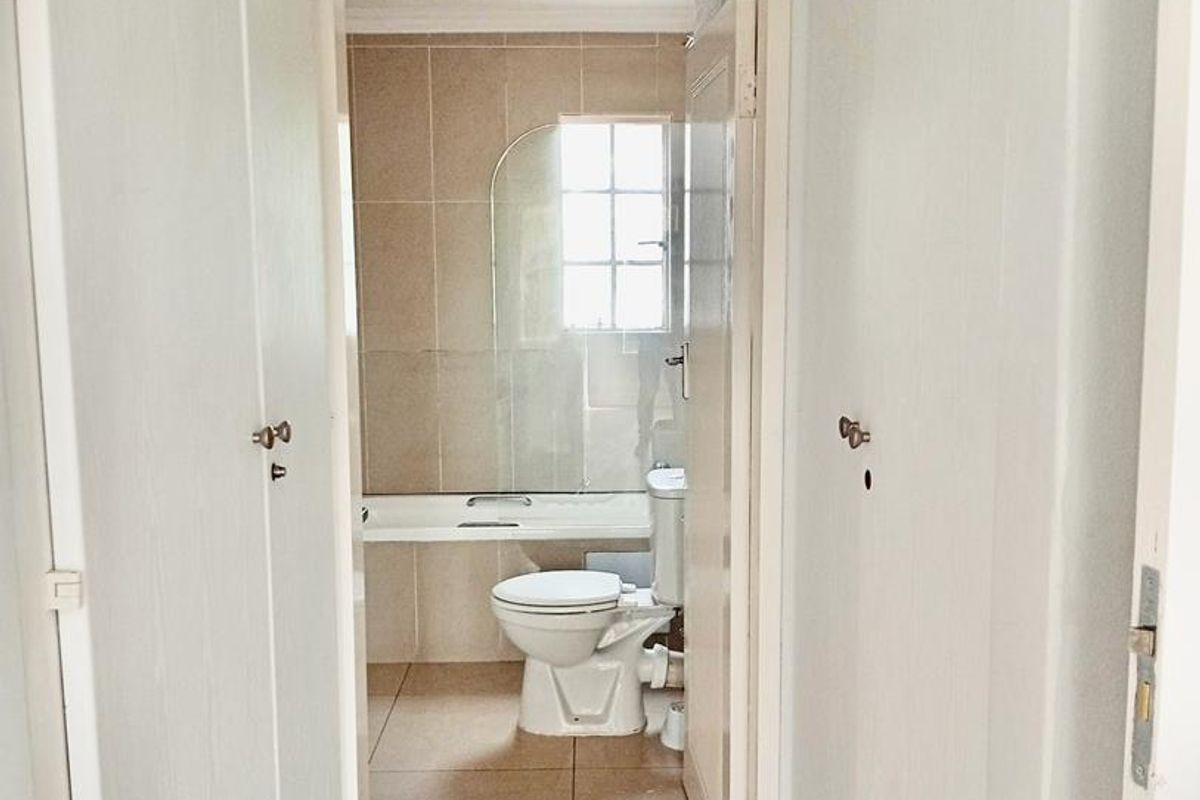 A view through a hallway into a functional bathroom featuring a bathtub, toilet, and neutral wall and floor tiling.