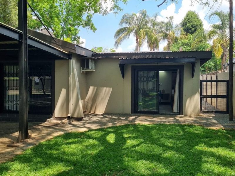 Rear exterior view of the apartment featuring a paved patio area, sliding glass doors, and established garden space.