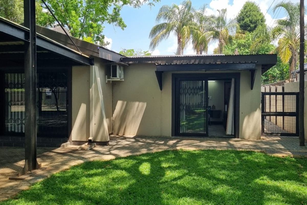 Rear exterior view of the apartment featuring a paved patio area, sliding glass doors, and established garden space.