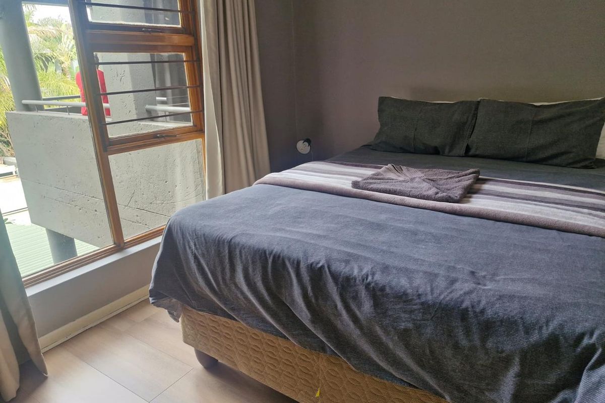A well-lit bedroom featuring wood-look flooring, large windows with natural light, and direct access to an outdoor balcony area.