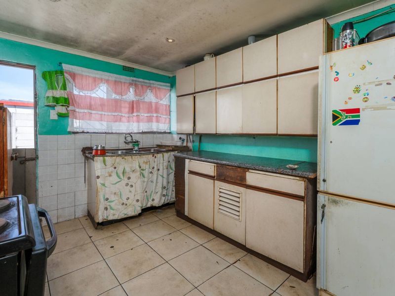 A dated kitchen featuring original built-in cabinetry, laminate countertops, and tiled flooring, requiring significant cosmetic updates and modernization.