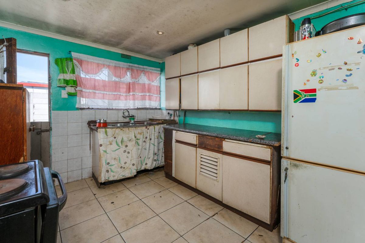 A dated kitchen featuring original built-in cabinetry, laminate countertops, and tiled flooring, requiring significant cosmetic updates and modernization.
