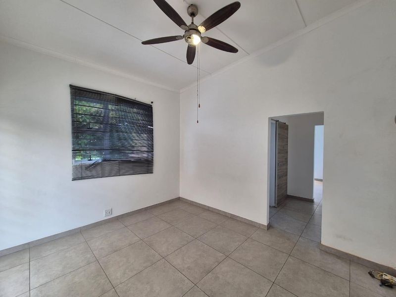 A bright, empty bedroom featuring neutral tiled flooring, a ceiling fan, and venetian blinds, offering a clean canvas for personalization.