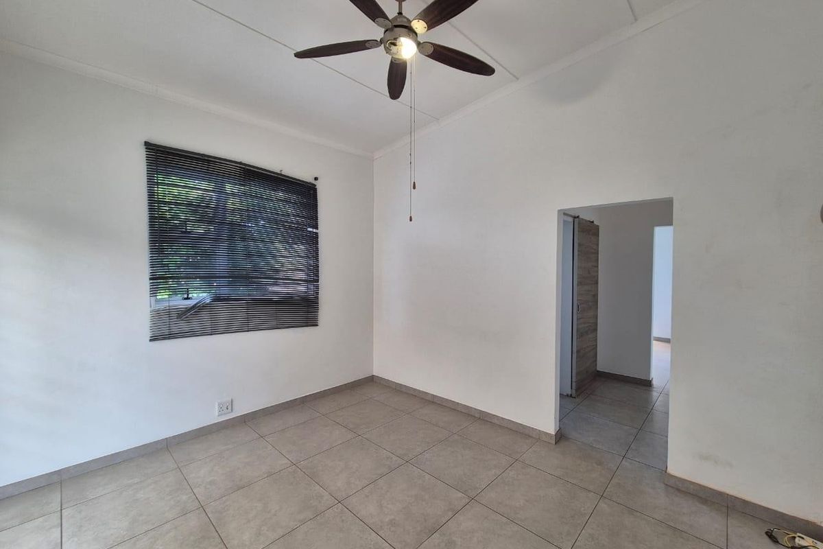 A bright, empty bedroom featuring neutral tiled flooring, a ceiling fan, and venetian blinds, offering a clean canvas for personalization.