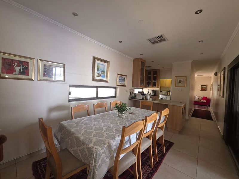 Open-plan dining area featuring tiled flooring, recessed lighting, and a functional kitchen with cabinetry and an island, leading into a hallway.