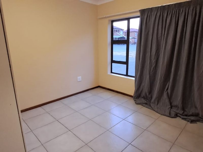 A vacant bedroom featuring neutral wall paint, tiled flooring, and a large window with curtain track, offering a clean and versatile living space.