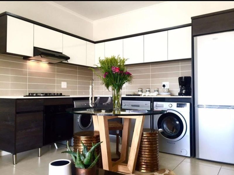 Modern kitchen featuring sleek two-tone cabinetry, tiled backsplash, built-in oven and hob, and integrated laundry appliances, offering a functional and contemporary cooking space.