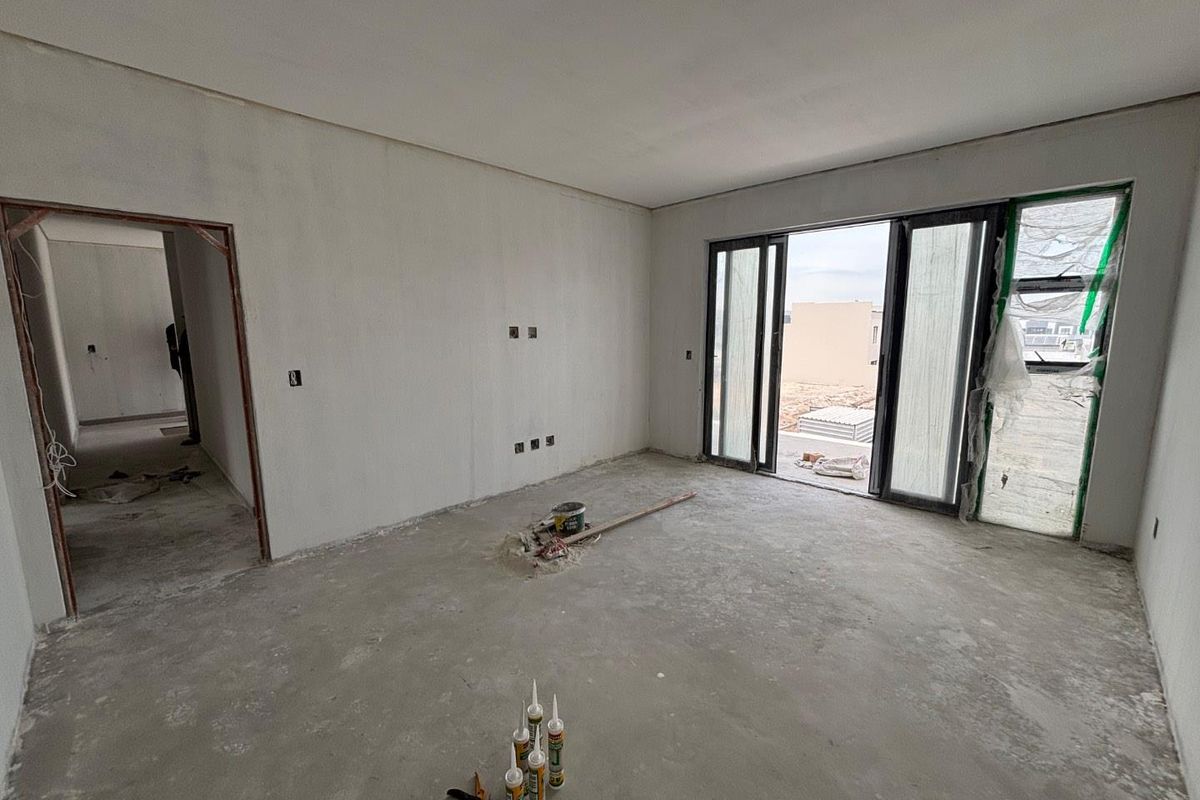 An unfinished living room space featuring bare concrete floors, unpainted walls, and sliding glass doors leading to an outdoor area.