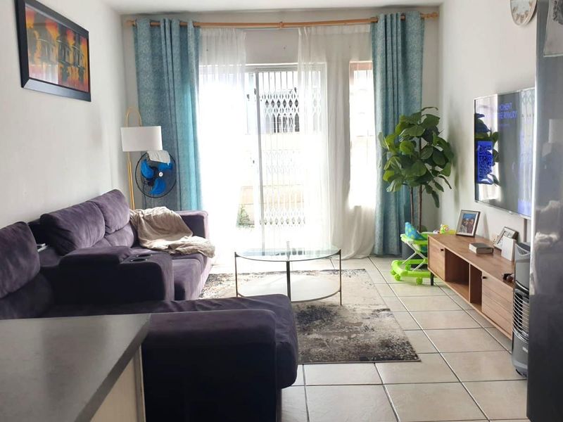 A bright living room featuring tiled flooring and a sliding glass door with a security gate, providing access to the exterior.