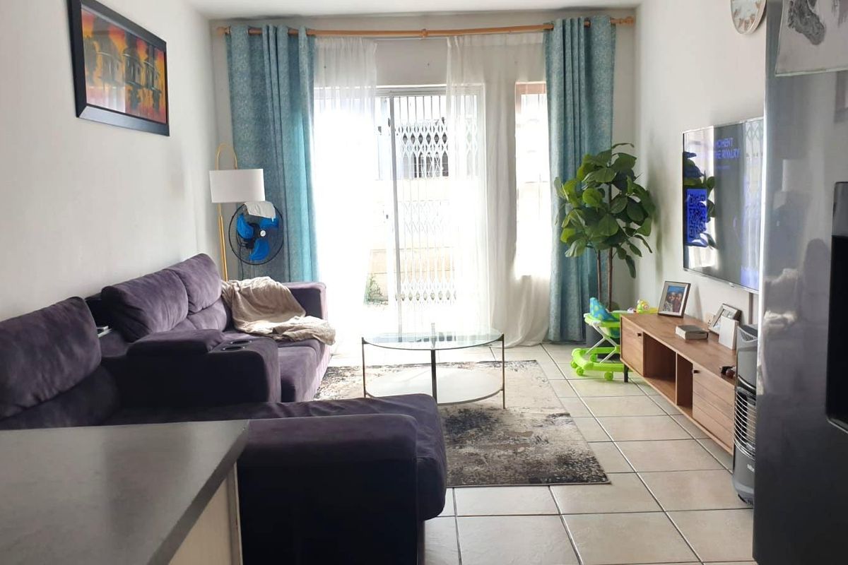 A bright living room featuring tiled flooring and a sliding glass door with a security gate, providing access to the exterior.
