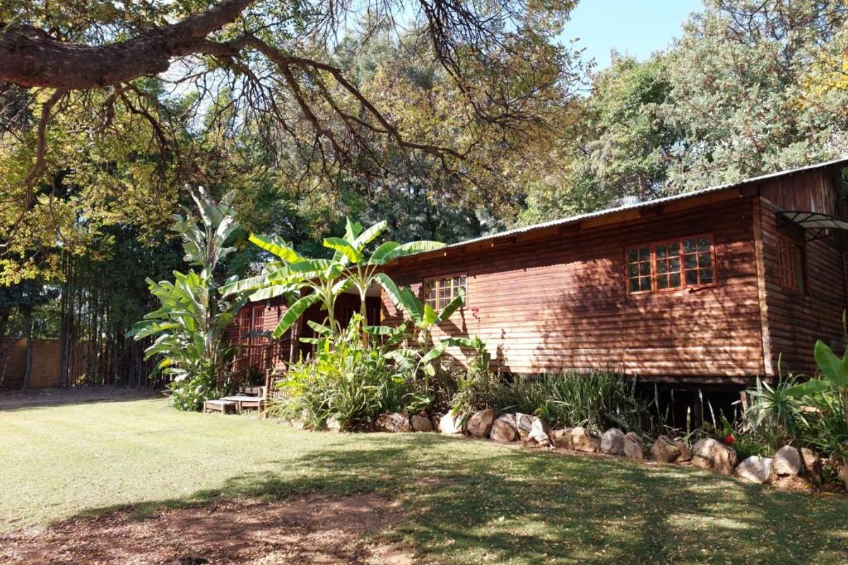 A rustic timber-clad house exterior featuring a raised deck, corrugated metal roof, and established garden surroundings in a tranquil, wooded setting.