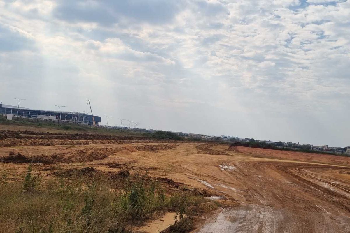 An expansive, undeveloped industrial land plot featuring cleared earth and distant views of existing commercial infrastructure.