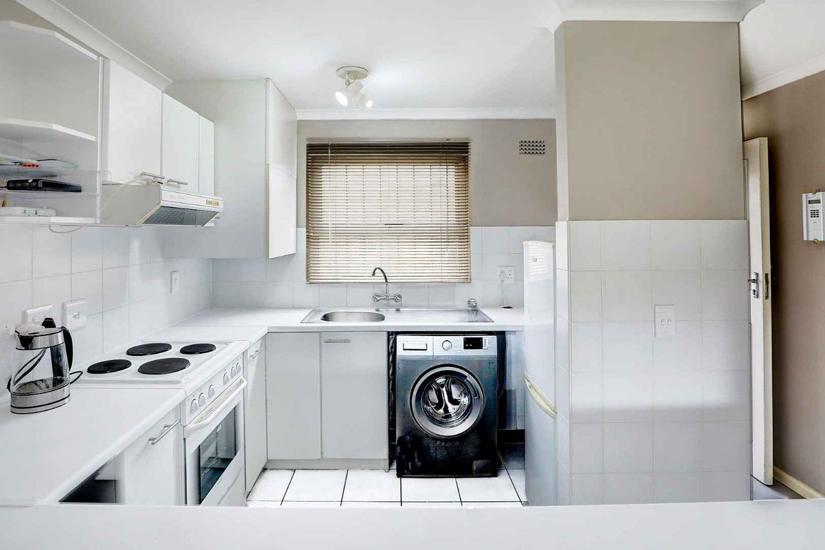 Functional kitchen featuring white cabinetry, tiled splashbacks, built-in oven with hob, extractor fan, and integrated laundry plumbing.