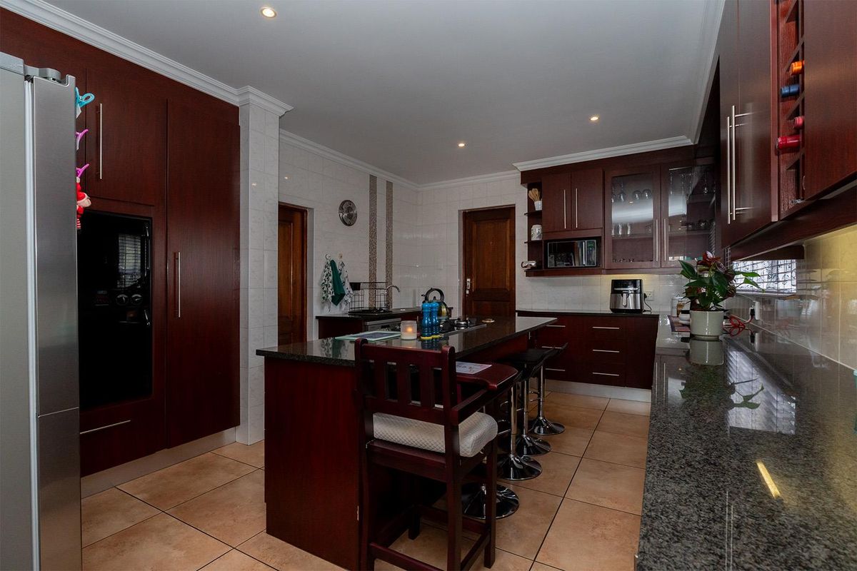 A well-appointed kitchen featuring dark wood cabinetry, granite countertops, a central island with breakfast bar seating, and recessed ceiling lighting.