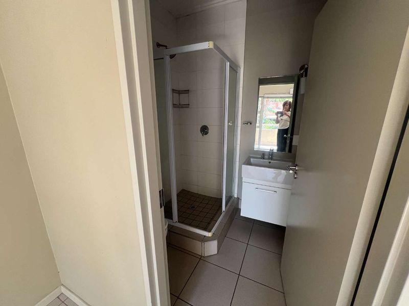 A compact bathroom featuring a shower enclosure, wall-mounted vanity with basin, and neutral floor tiling.