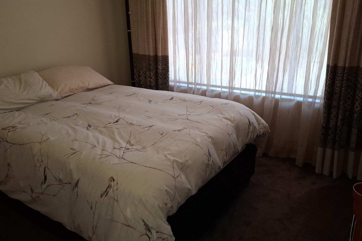 A bedroom featuring carpeted flooring and large windows with floor-to-ceiling curtains, providing natural light to the space.