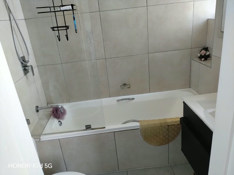 A modern bathroom featuring a built-in bathtub with a glass shower screen and neutral wall tiling.