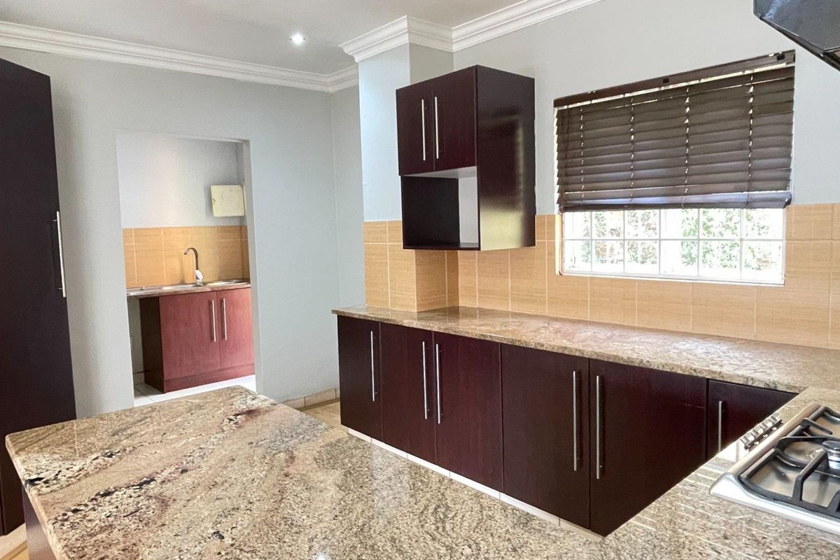 Modern kitchen featuring dark wood cabinetry, granite countertops, a gas hob with extractor, and a separate scullery area with additional sink and storage.