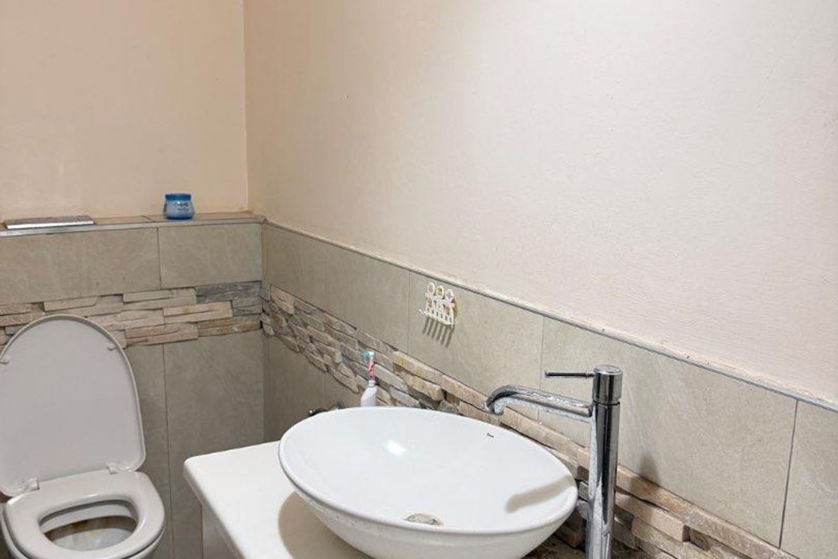 A functional bathroom featuring a modern vessel sink vanity, stone-look tile backsplash, and a standard toilet.