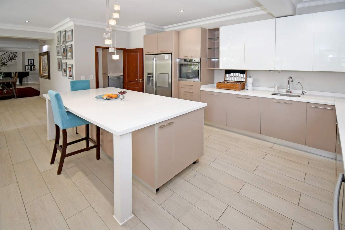Modern kitchen featuring a large central island, sleek two-tone cabinetry, integrated oven, and light-toned tiled flooring.