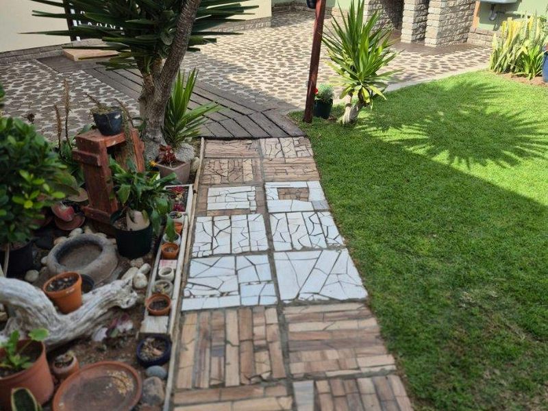 Rear garden area featuring a built-in brick braai, outdoor sink, lawn, and a decorative paved walkway.