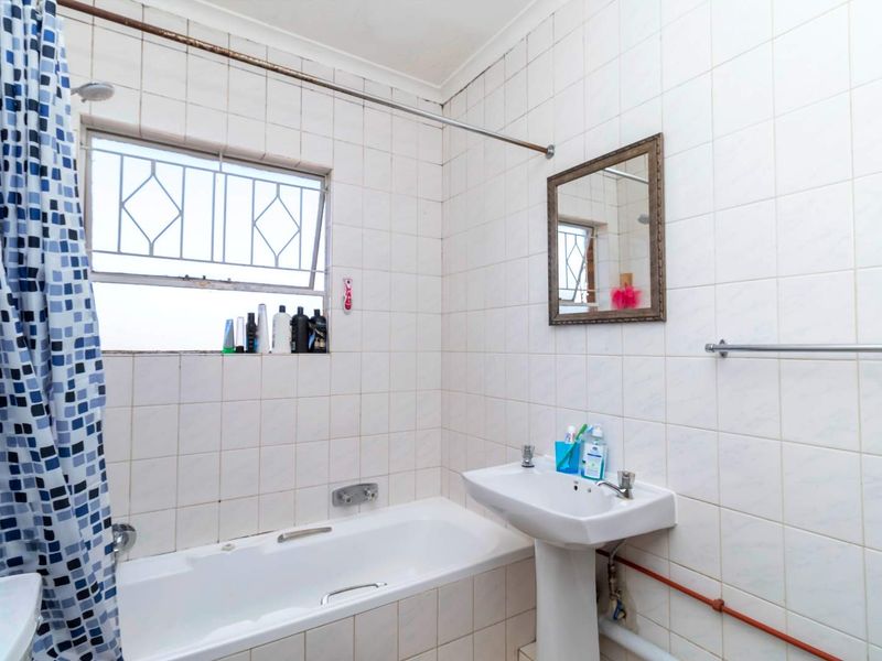 A functional bathroom featuring a white bathtub, pedestal basin, and full-height wall tiling with a window for natural ventilation.
