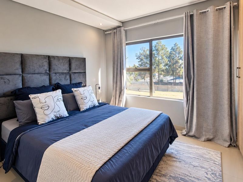 A well-maintained bedroom featuring a built-in wardrobe, neutral wall finishes, and large windows providing natural light.