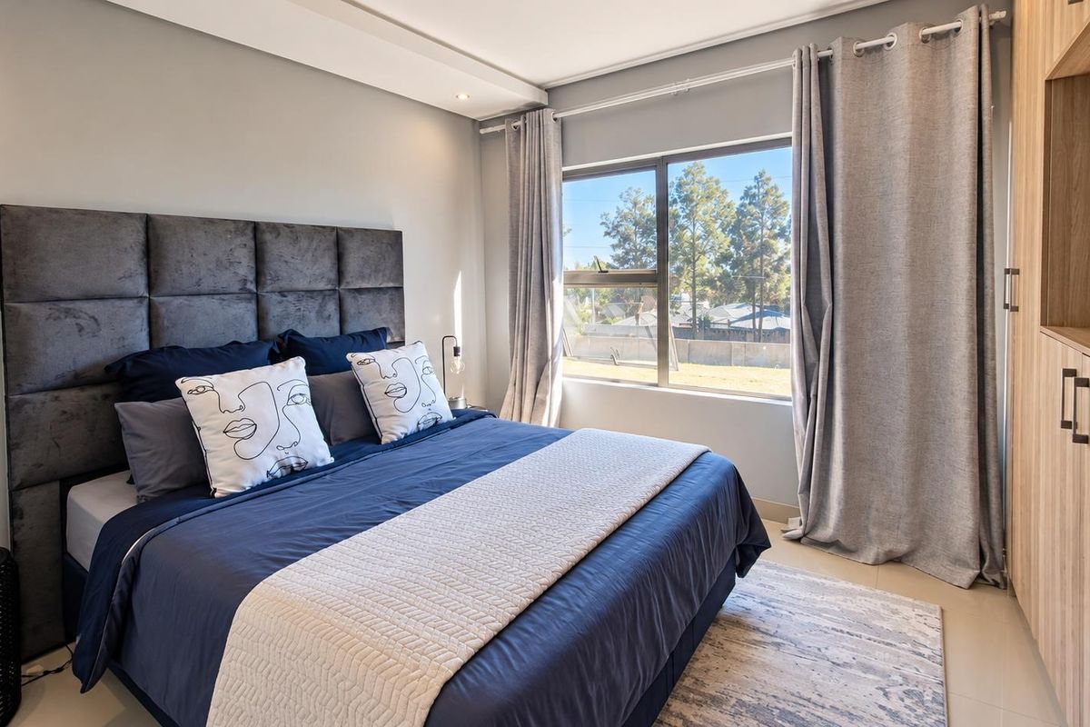 A well-maintained bedroom featuring a built-in wardrobe, neutral wall finishes, and large windows providing natural light.