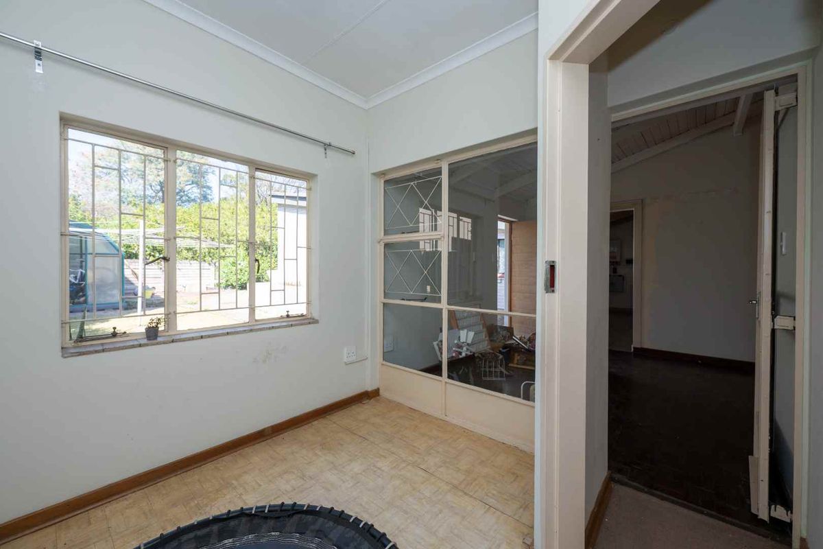 An empty living area featuring vinyl flooring, a glass partition wall, and large windows with security bars, offering a blank canvas for renovation.