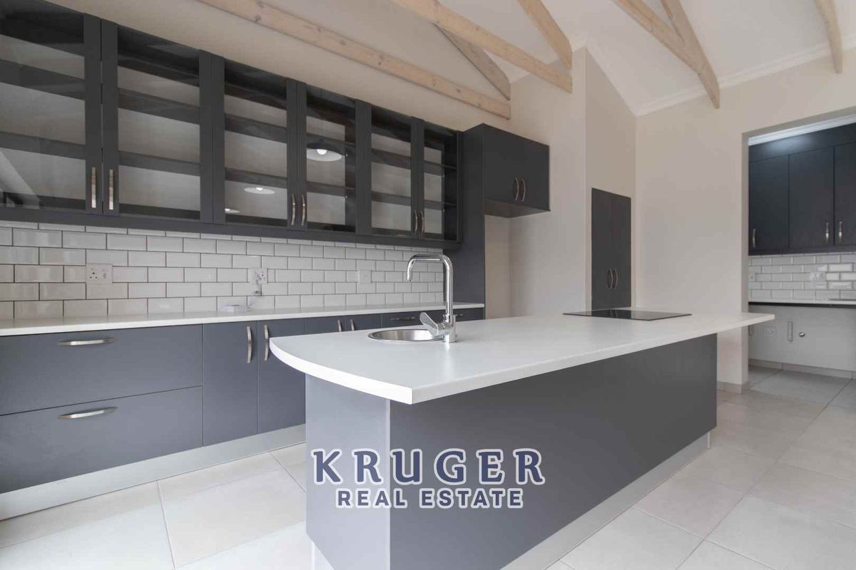 Modern kitchen featuring dark grey cabinetry, white stone countertops, subway tile backsplash, and exposed timber ceiling beams, with an adjacent scullery area.