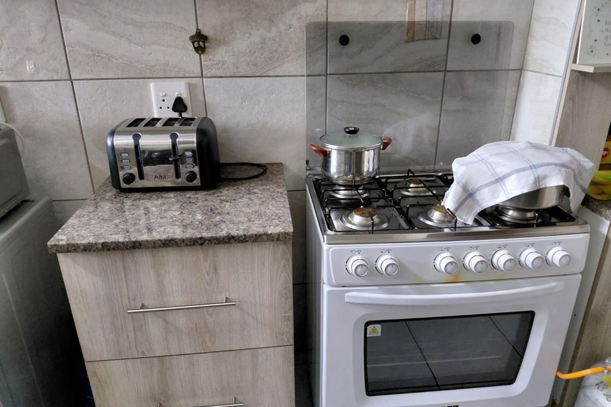 A compact kitchen area featuring a gas stove with oven, granite countertop, and light wood-finish cabinetry with a tiled backsplash.