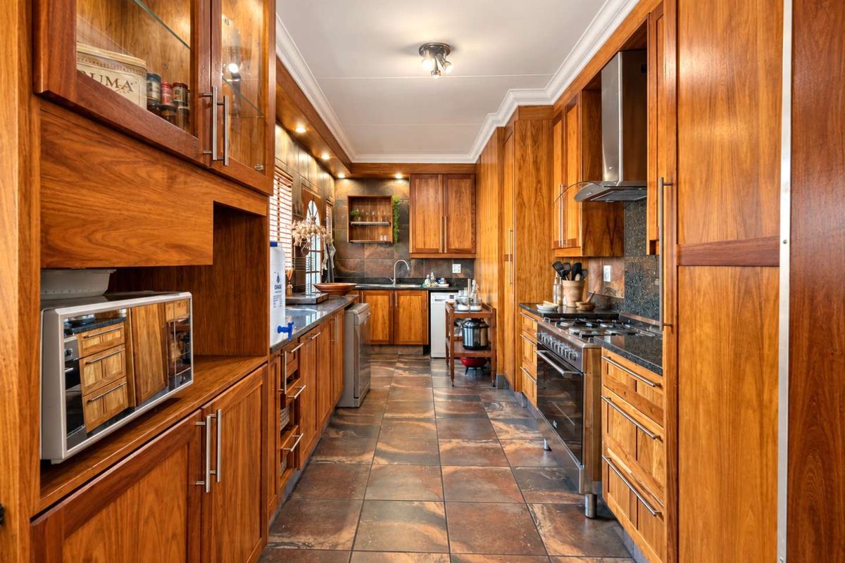 A well-maintained kitchen featuring extensive wooden cabinetry, granite countertops, a gas stove with extractor fan, and durable tiled flooring.