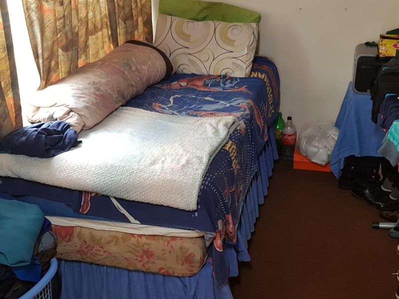 A compact bedroom space featuring a single bed and window with curtains.