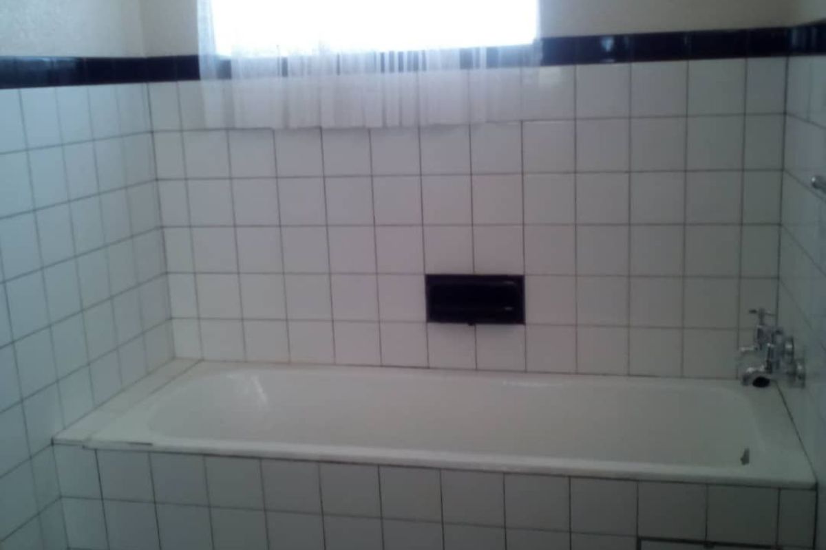 A dated bathroom featuring a built-in bathtub with white square wall tiles and a contrasting black border tile detail.