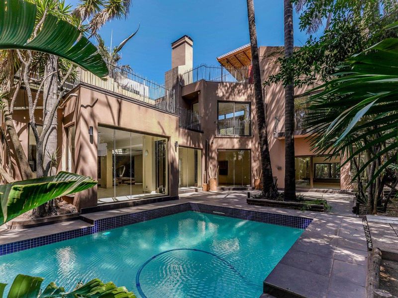 Rear exterior view of a multi-level home featuring a swimming pool, tiled patio area, and large glass sliding doors leading into the living spaces.