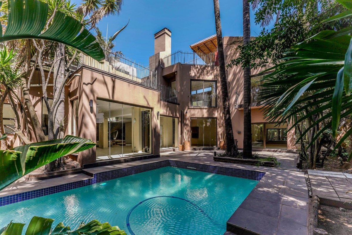 Rear exterior view of a multi-level home featuring a swimming pool, tiled patio area, and large glass sliding doors leading into the living spaces.